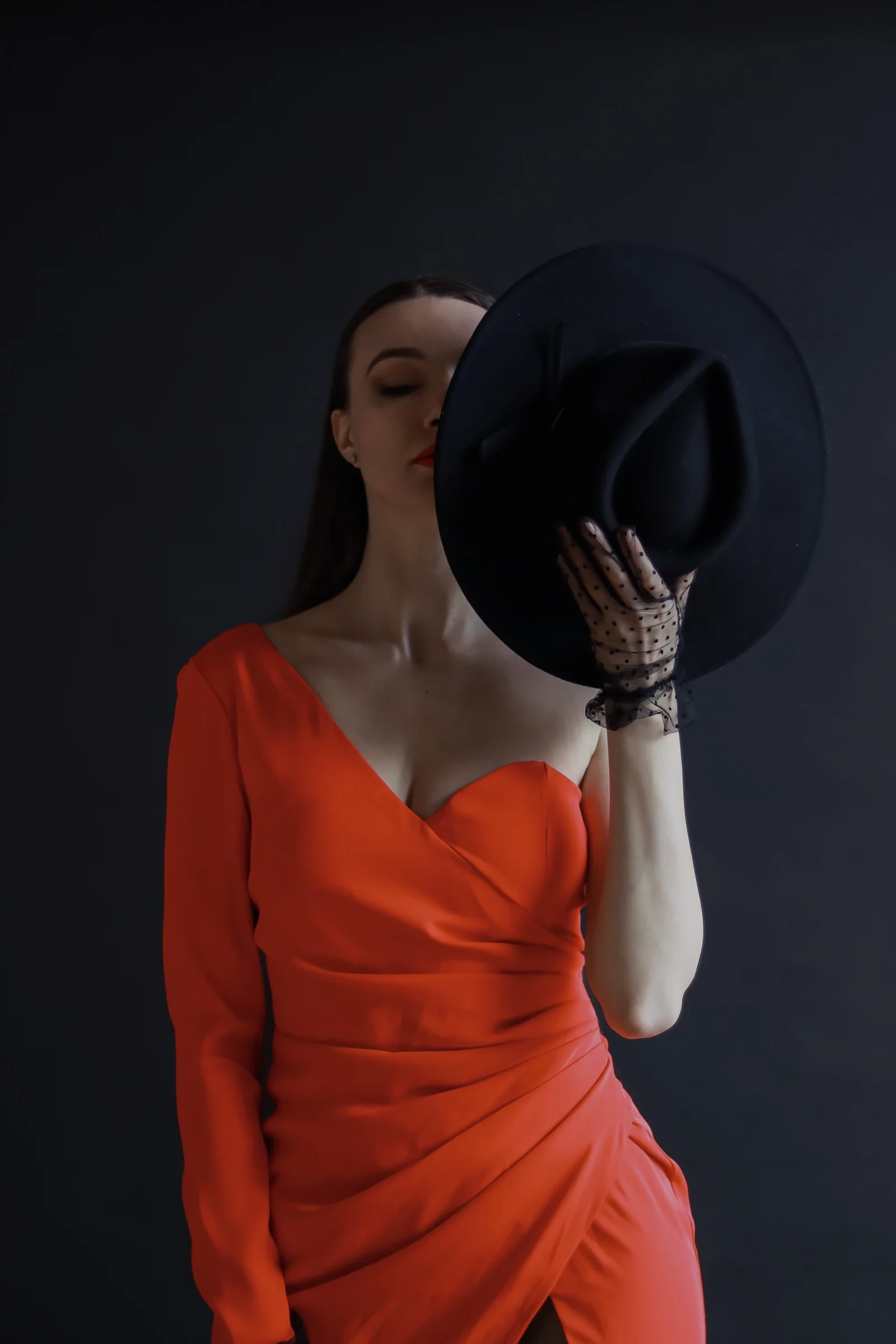 Designer in a red gown holding a black hat